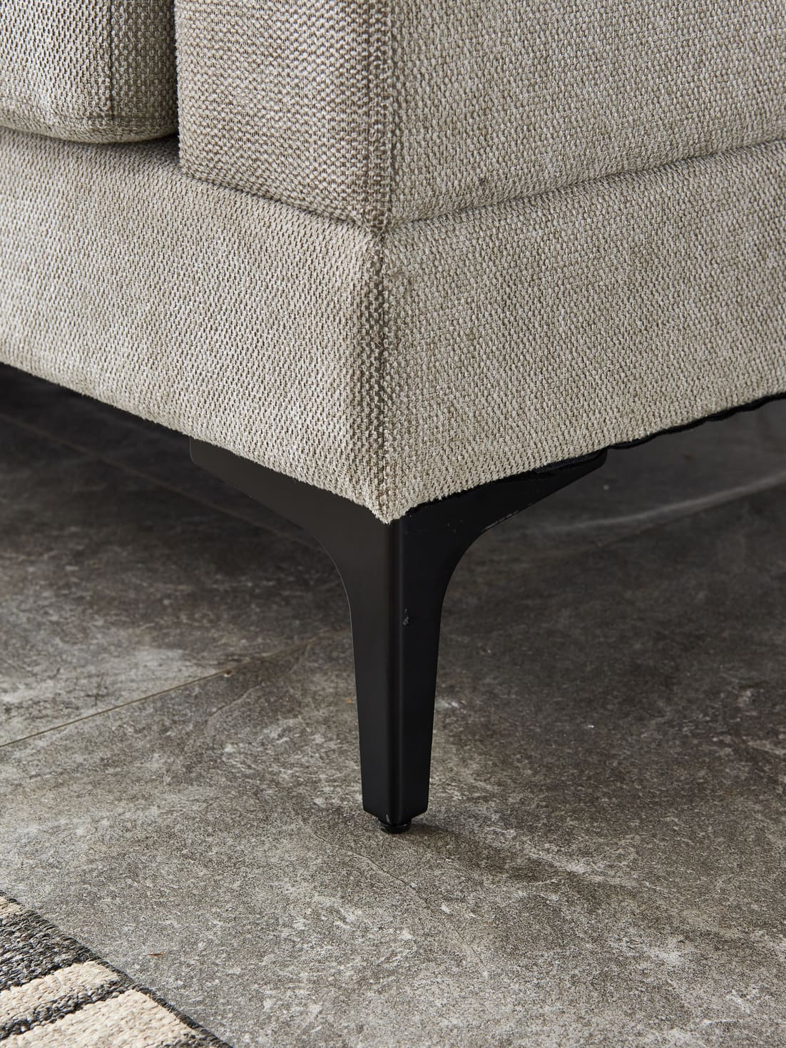 Anek three seater grey fabric sofa with black metal legs on concrete floor, close-up detail view