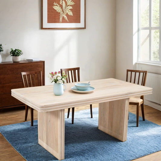 Hudson Carved Mango Wood Dining Table with ribbed base design on blue rug, styled with chairs and decorative accents